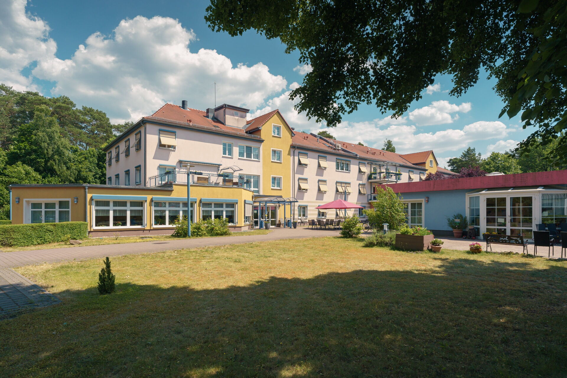 Wohnanlage. Großes Haus mit einer Terrasse davor. Wiese davor.