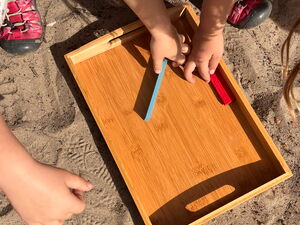 Von oben. Kinder mit einem Holztablett im Sand.