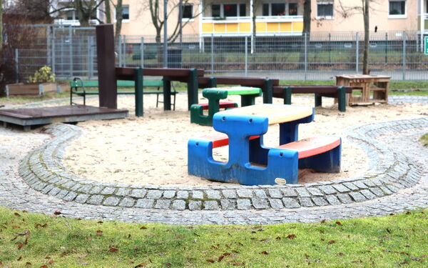 Spielgeräte vor einer Kita. Farbige Sitzgelegenheiten, Sandkasten, Wasserspielplatz.