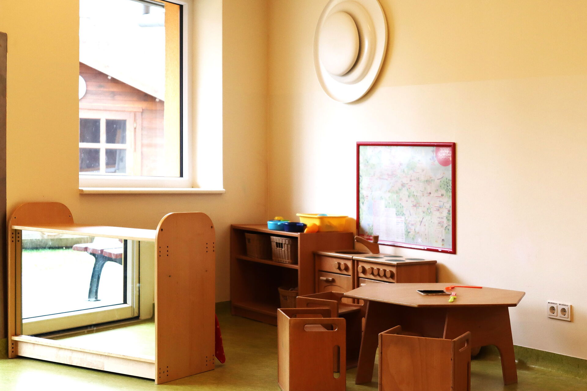 Heller Raum, in der Ecke eine kleine Spiel-Küche mit Spühle, Herd, Tisch und Stühlen aus dunklem Holz für kleine Kinder.