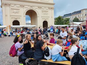 Großer Platz mit vielen Menschen und unterschiedlichen Ständen von Vereinen. AWO Potsdam, Kultür Potsdam. An einer Biertischgarnitur im Vordergrund sitzen Jugendliche die Eis essen.