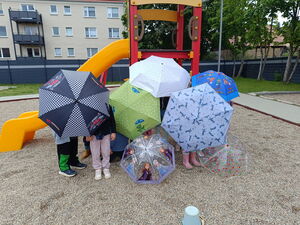 Kinder auf einen Spielplatz vor einer Rutsche. Viele bunte Regenschirme verdecken die Kinder.