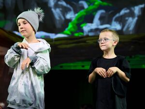 Zwei Jungen auf der Bühne. Ein Junge mit grauer Mütze und grauem Kapuzenpulli. Der zweite Junge trägt ein Brille und ein schwarzes T-Shift. Beide haben die Hände vor dem Körper.