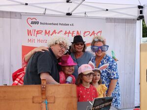 Fotobox. 4 Erwachsene, 2 Mädchen mit bunten Accessoire, wie Perücke, pinker Hut, schwarzer Hut, eine riesige Sonnenbrille, ein Mädchen hat Häschen-Ohren.