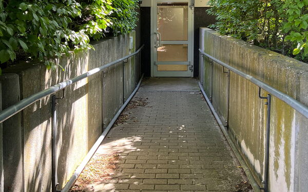 Eine Rampe mit Geländer auf beiden Seiten führt hinab zu einer Tür.