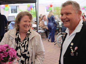 2 fröhliche Menschen die in die Kamera lachen. Vorne links in der Ecke sind pinke Blumen.