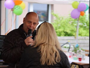Interview: Mann sagt etwas in ein Mikro. Blonde Frau steht vor ihm, mit Rücken zur Kamera.