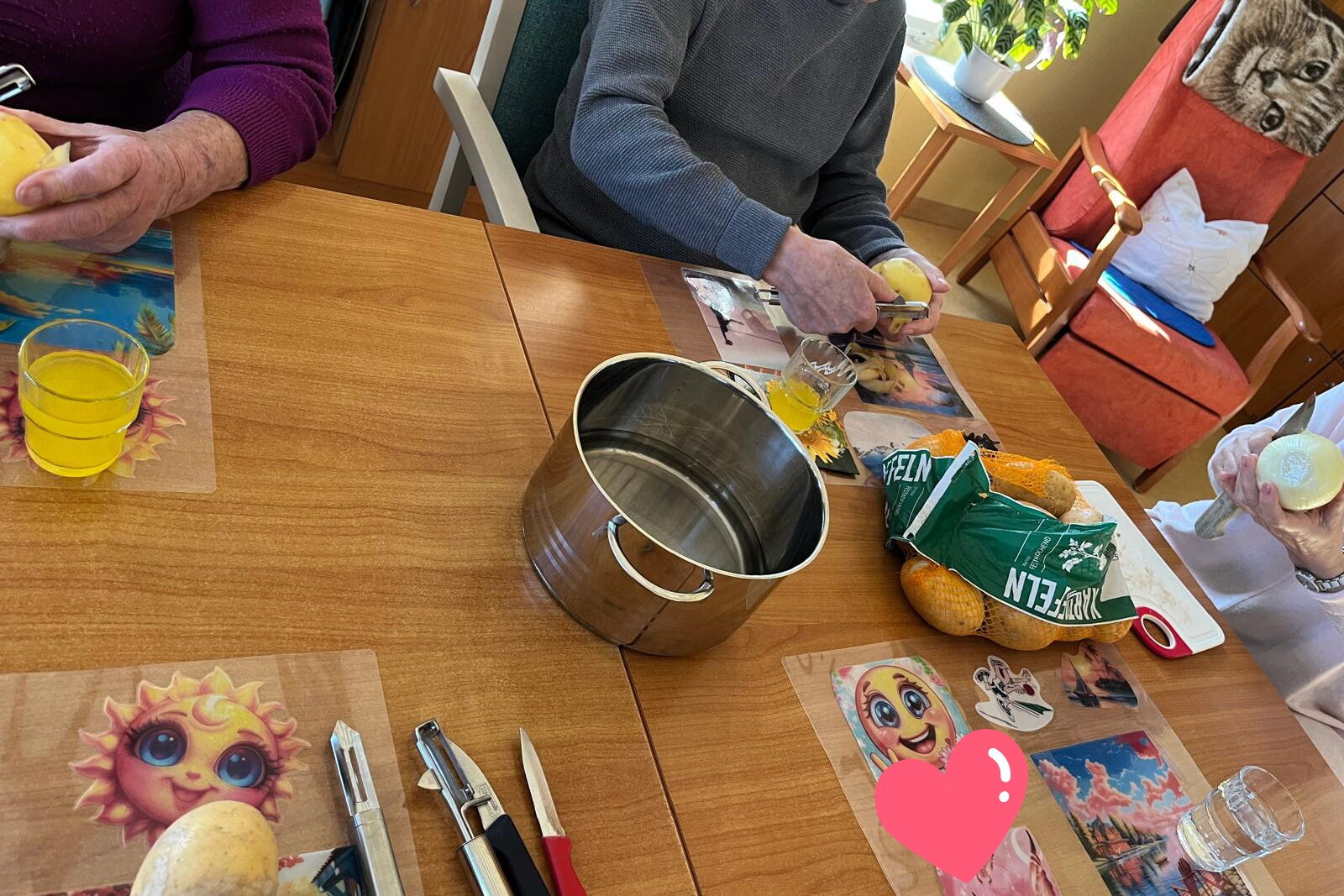 Senioren beim Kartoffeln schälen. In der Mitte auf dem Tisch steht ein leerer Topf.