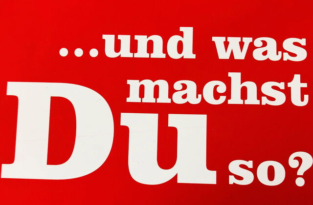 Rote Schrifttafel mit weißer großer Schrift. Der Werbetext der AWO Ehrenamtsagentur fragt: ... und was machst Du so?