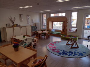 Zimmer mit mehreren Tischen und Spielteppich.