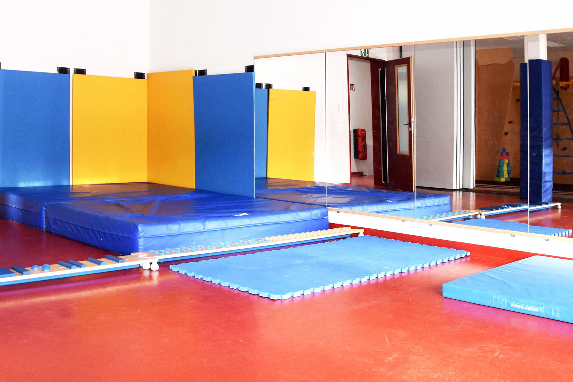 Sportraum. Große Spiegel an der Wand, davor liegen blaue Matten.