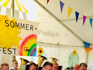 Wimpel und Plakat mit Sonne und Regenbogen Aufschrift: Sommerfest. Über den Köpfen der Blaskapelle.