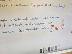Flipchart Papier auf dem unten steht: "Manche Medikamente werden in der Apotheke nicht verkauft, weil manchmal nur der Mensch den Menschen heilt."