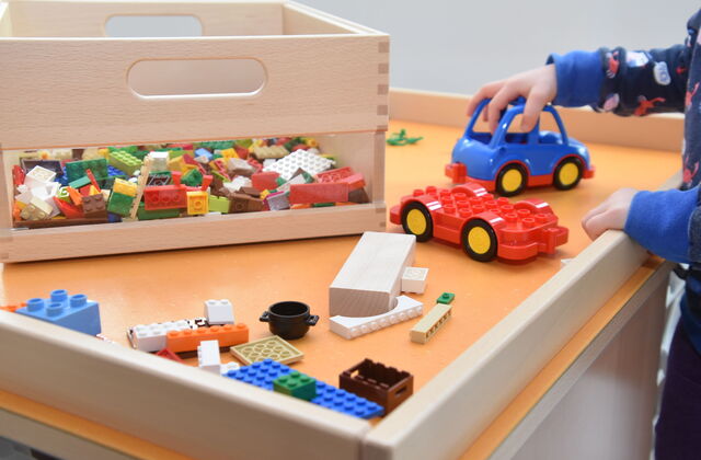 Spieletisch mit Lego und keinem Auto. Eine Kinderhand schiebt das kleine blaue Auto.