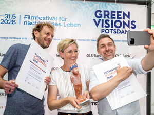 Die Preisträger bei einem Versuch, ein Selfie zu machen. Zwei Männer, eine Frau in der Mitte mit Urkunden und Skuptur. Mann rechts hält das Handy mit Abstand vor sich.