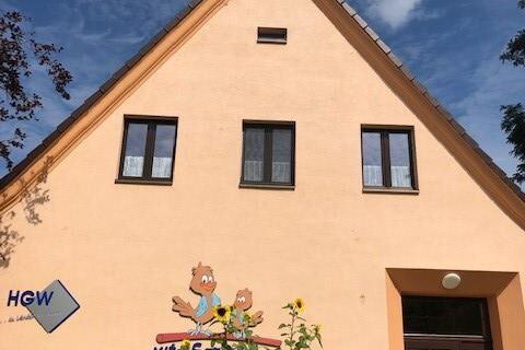 Ein Haus mit Spitzdach und heller Fassade. An dem Haus ist ein Schriftzug:  Kita Spatzenhaus       darüber das Bild von zwei Spatzen.