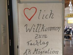 Im Eingangsbereich. Flipchart mit Text: Herzlich willkommen zum Fachtag AK Migration (West) Havelland.