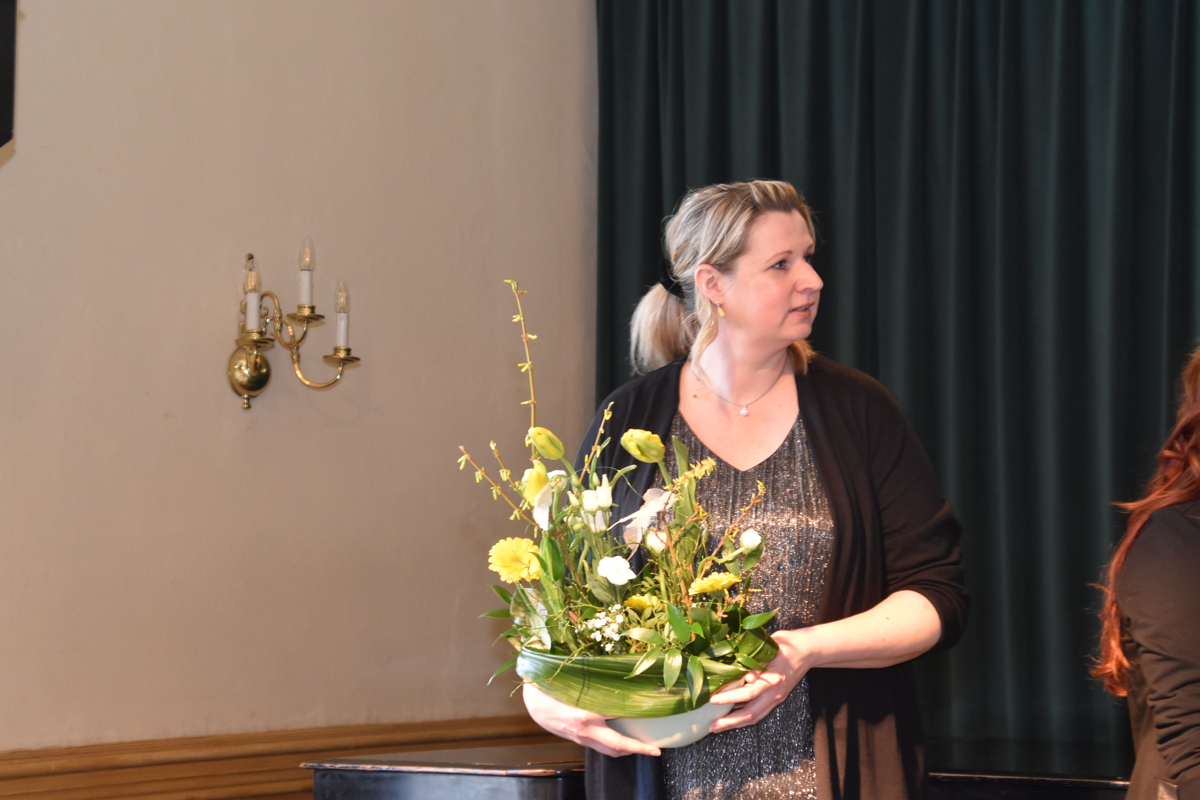 Eine Frau hält großes Blumengesteck in Glasschale in den Händen