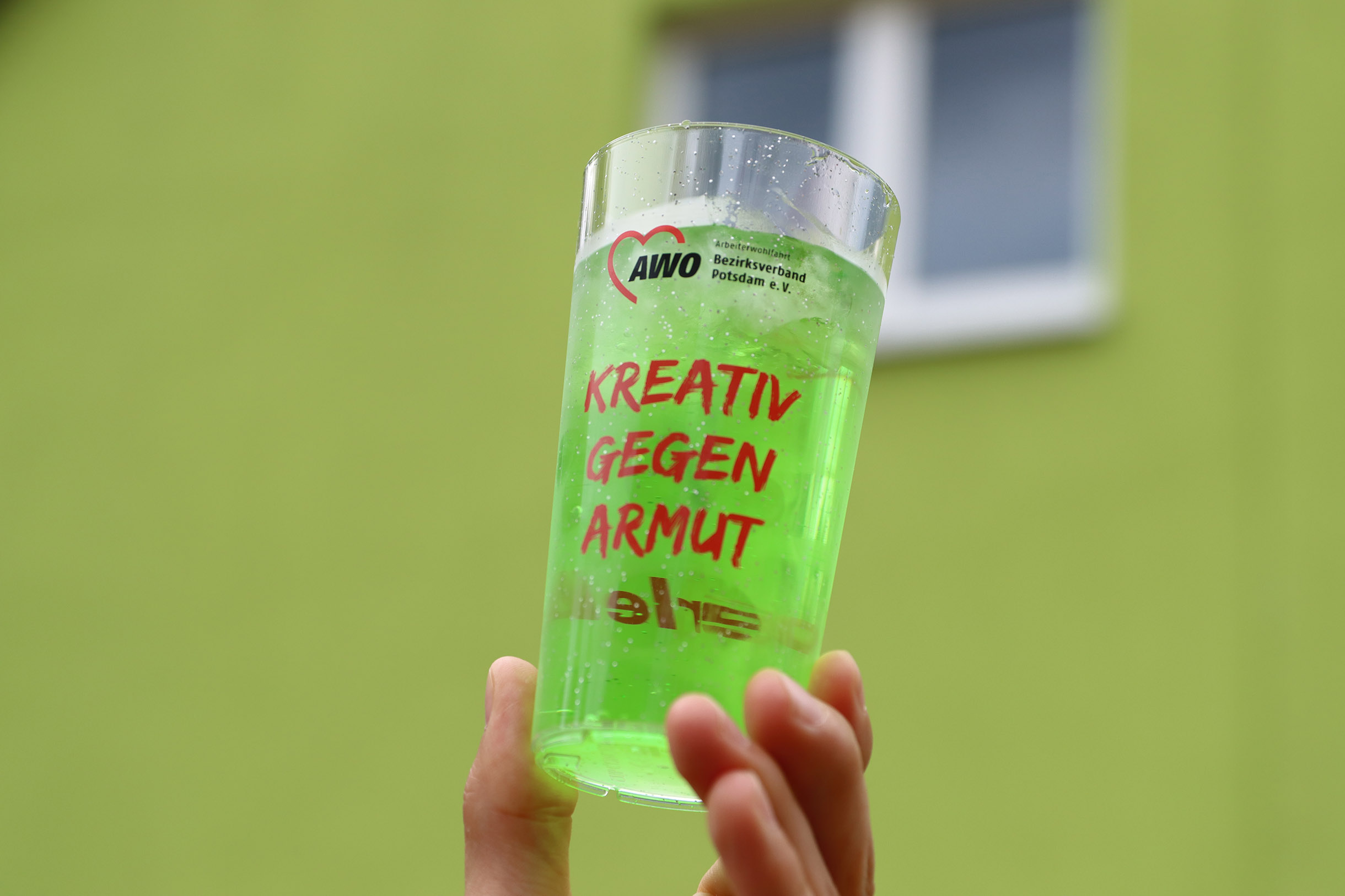 Giftgrünes Slush-Eis in einem AWO Plastebecher mit Aufschrift: Kreativ gegen Armut.