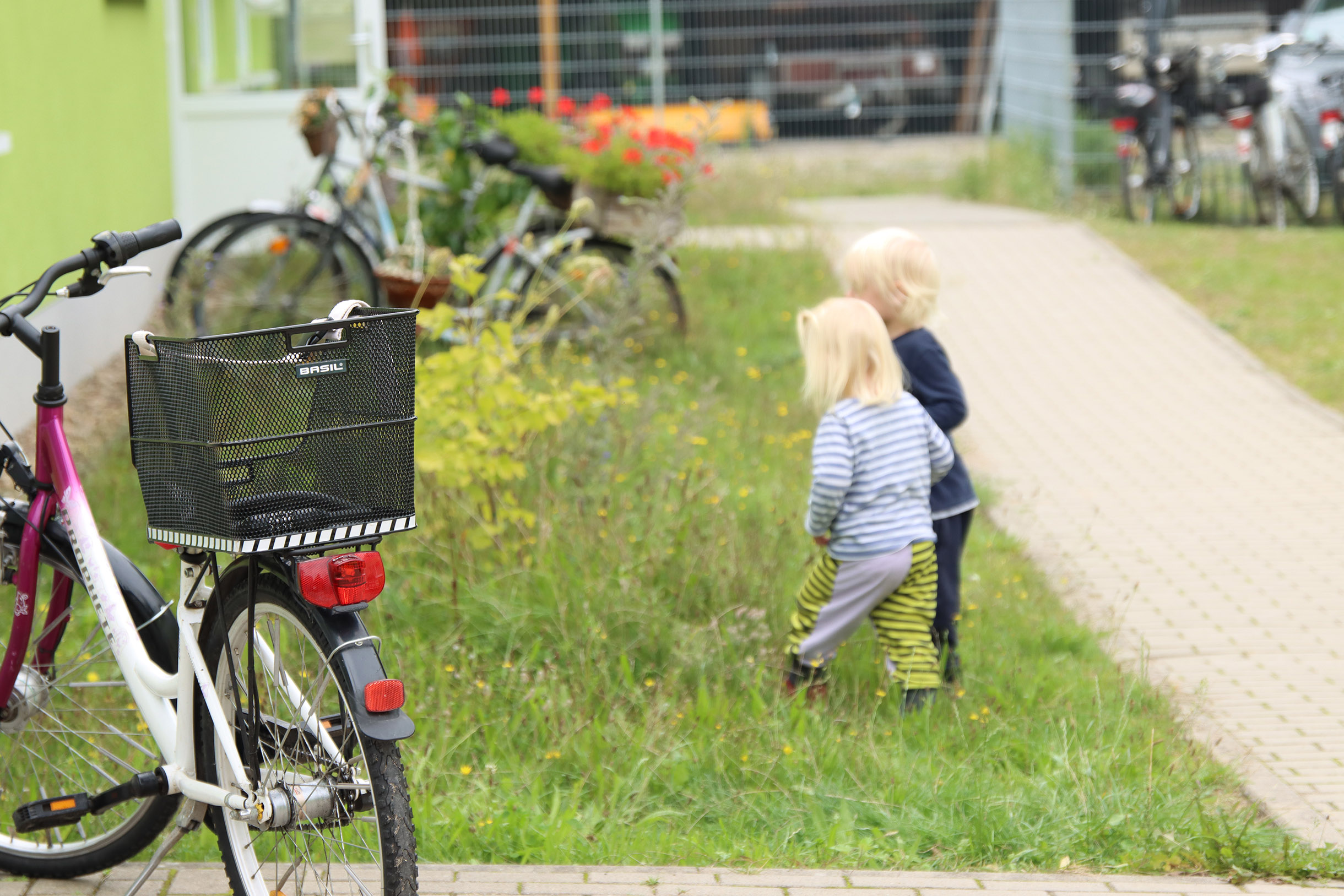 Abgestellte Fahrräder. an einem grünen Gebäude. Zwei kleine Kinder, beide hellblond.