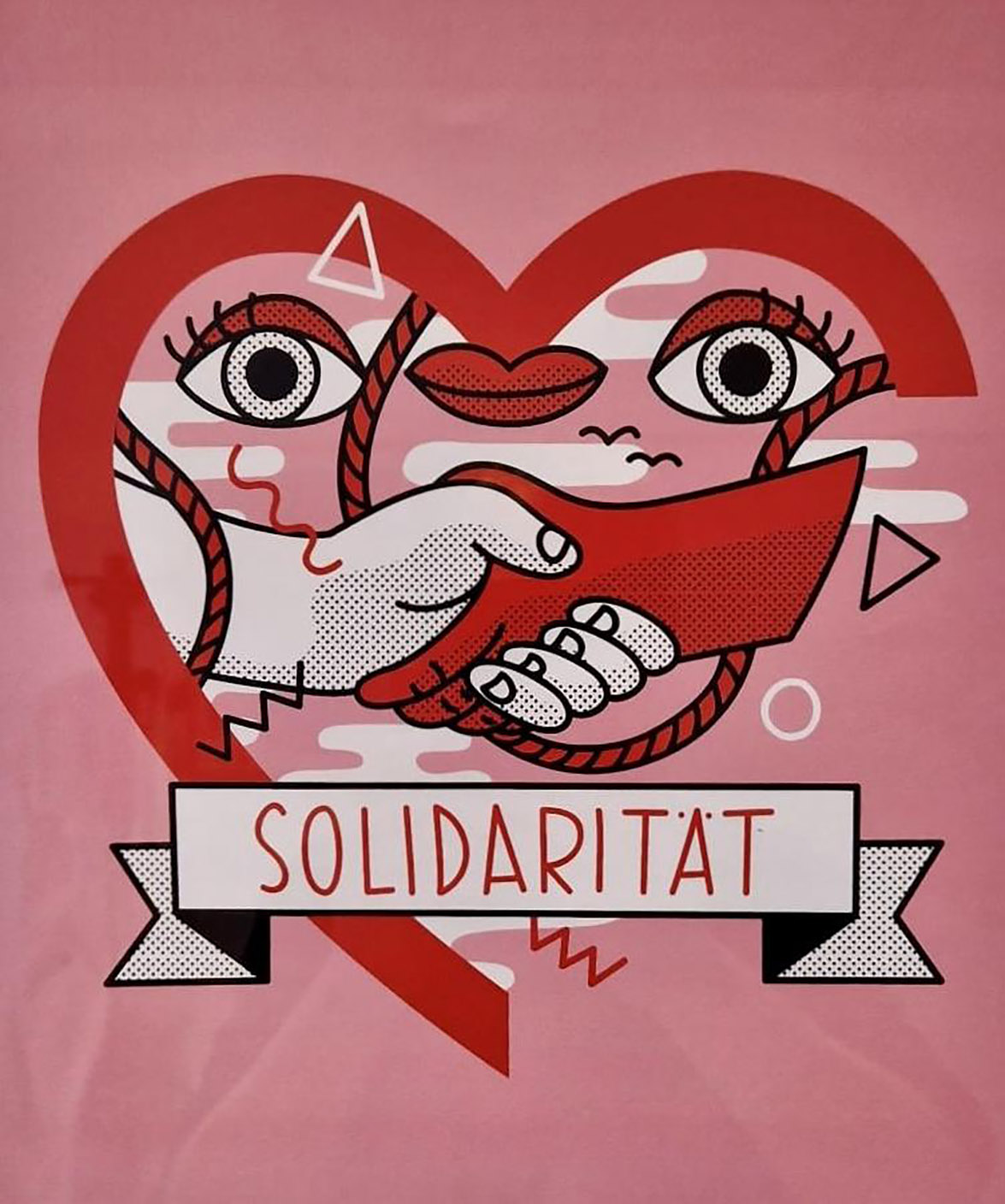 Plakat: Rosa, rotes Herz, zwei Hände die sich die Hand geben, eine rot und die andere weiß, zwei Augen und ein Mund in der Herzform. Darunter steht in Großbuchstaben: Solidarität