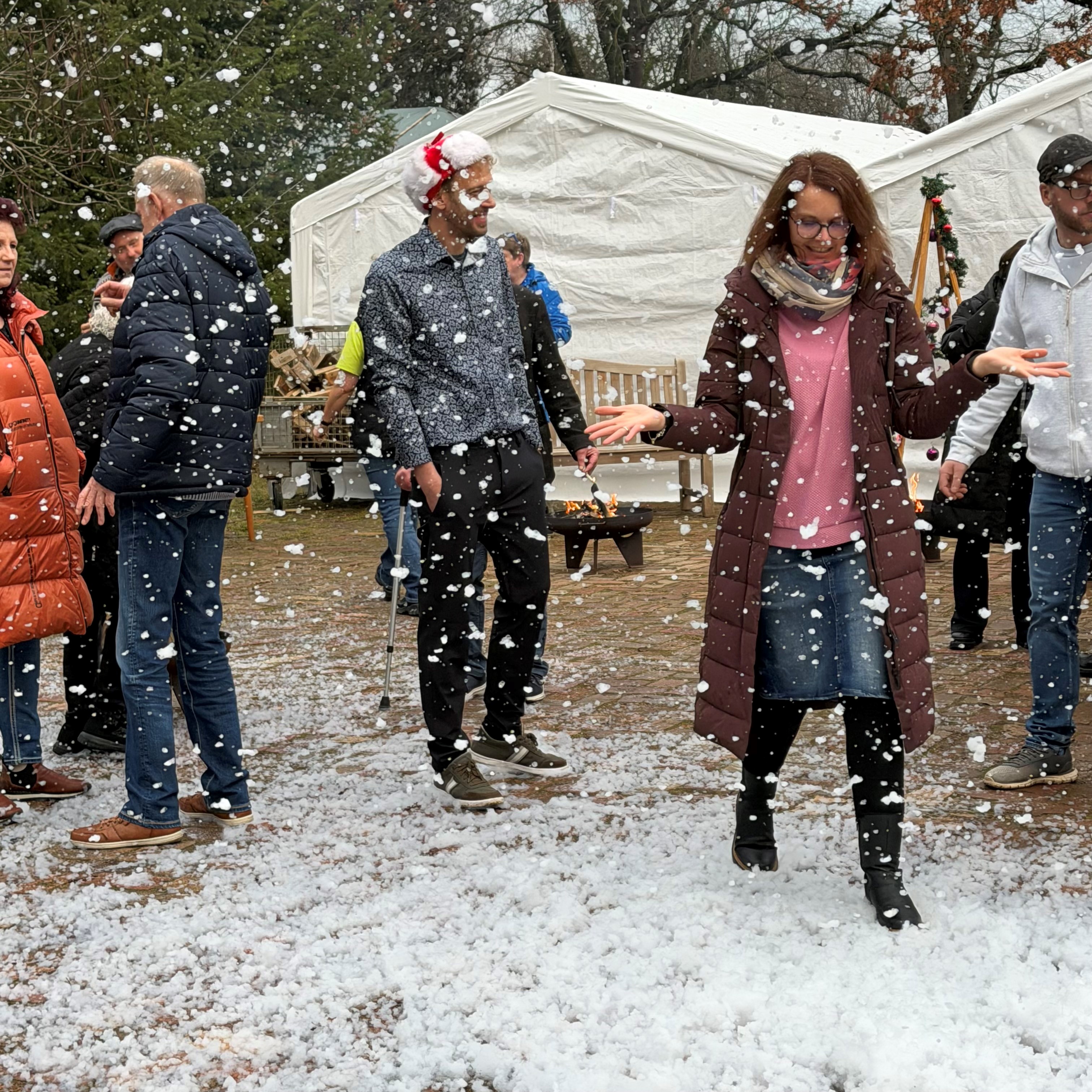 Menschen freuen sich über Kunstschneegestöber. Weiße Flocken am Boden.