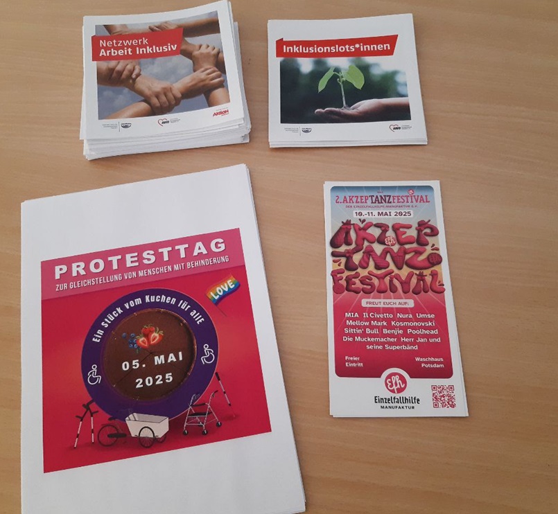Flyer auf einem Tisch. Vom Netzwerk Arbeit inklusiv, von den Inklusionslotsen, vom Protesttag Ein Stück vom Kuchen für alle und vom Akzeptanzfestival