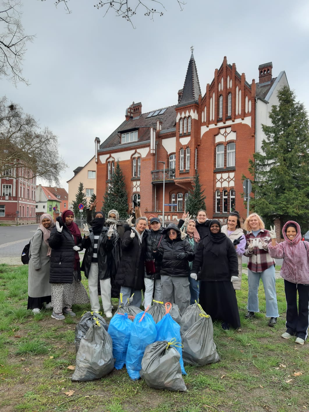 auf dem Bild sind mehrere Frauen aus verschiedenen Herkunftsländern vor dem Gebäude des interkulturellen Familiencafés und lachen in die Kamera. Vor ihnen sind mehrere volle Müllsäcke, die gesammelt wurden
