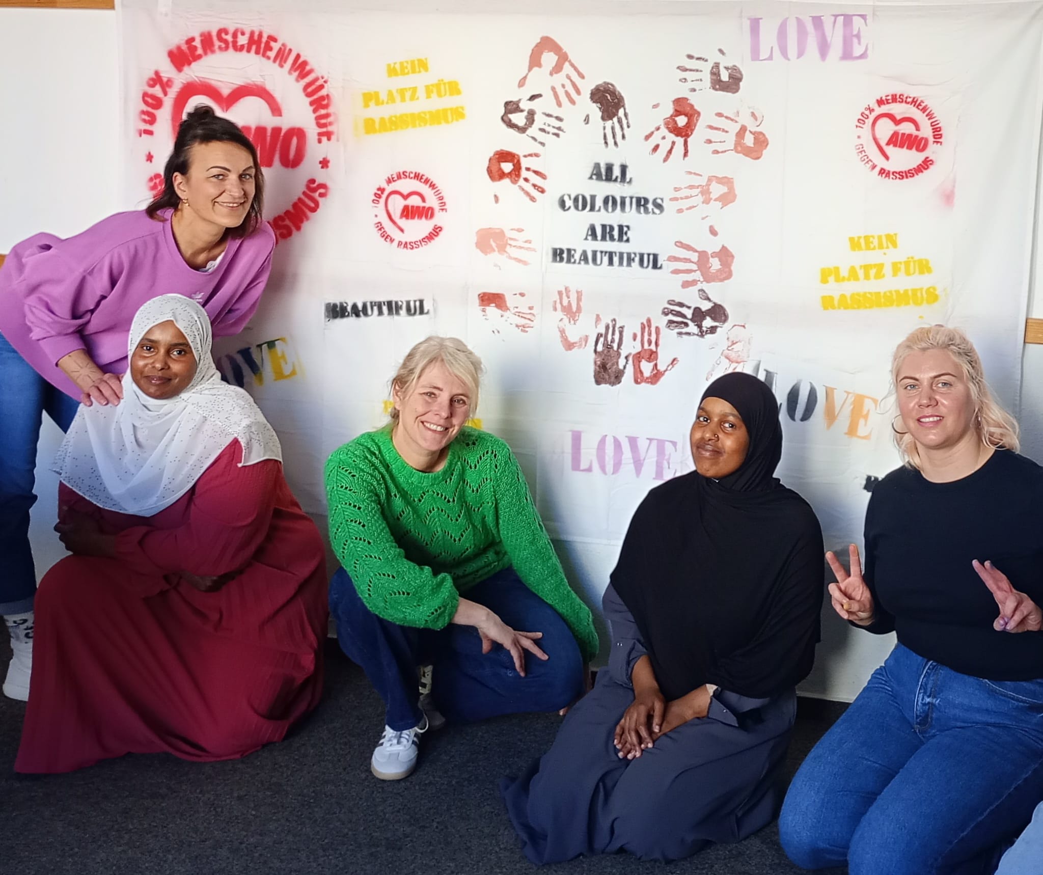 Mitarbeiterinnen und Besucherinnen des interkulturellen Familiencafés vor einem selbst gestalteten Plakat mit Schriftzügen, die ein Zeichen setzen gegen Rassismus und für Vielfalt