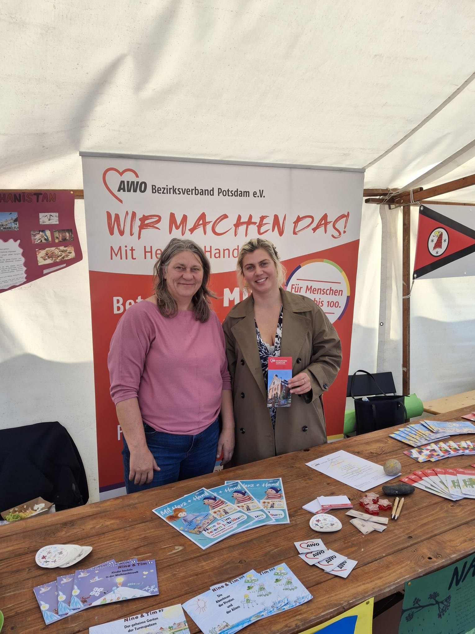 das Bild zeigt zwei Mitarbeiterinnen des interkulturellen Familiencafés , wie sie an einem Stand der AWO stehen und Flyer präsentieren