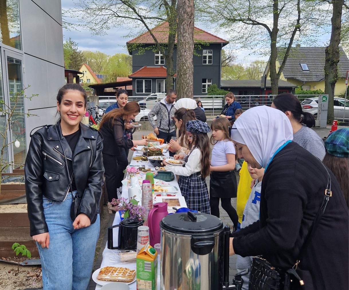 Viele Menschen stehen vor einem langen Tisch mit vielen Speisen zur Feier des Zuckerfest im EKiZ