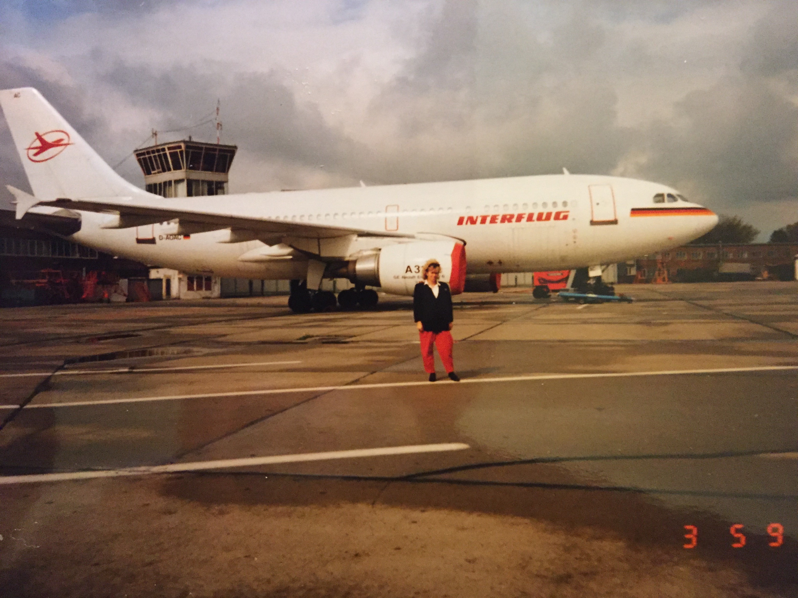 Historisches Foto mit Interflug-Flugzeug am Flughafen Schönefeld, vorn eine Person mit roter Hose und schwarzer Jacke.