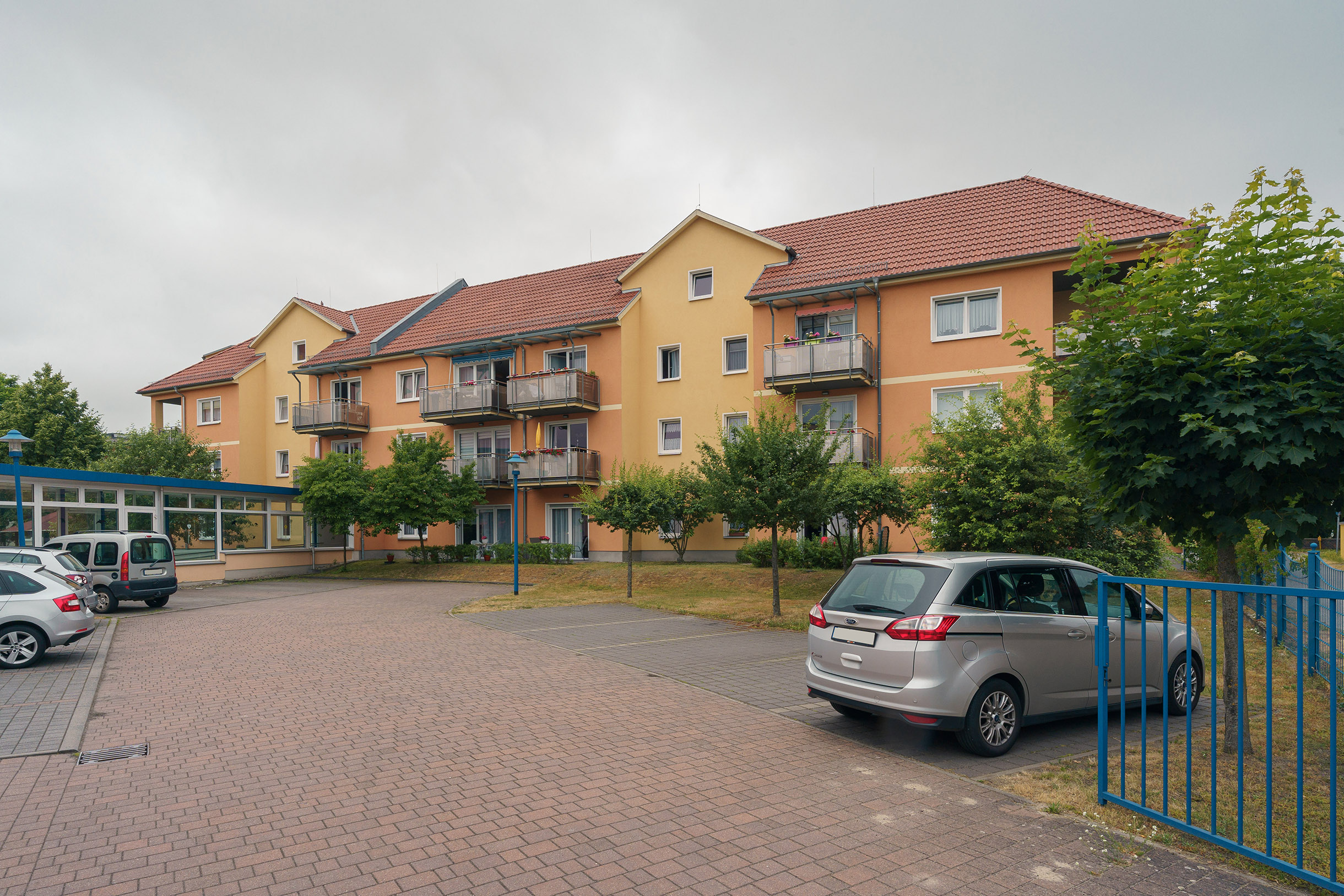 Parkplatz, parkende Autos, ein orangenes Wohngebäude mit Balkonen.