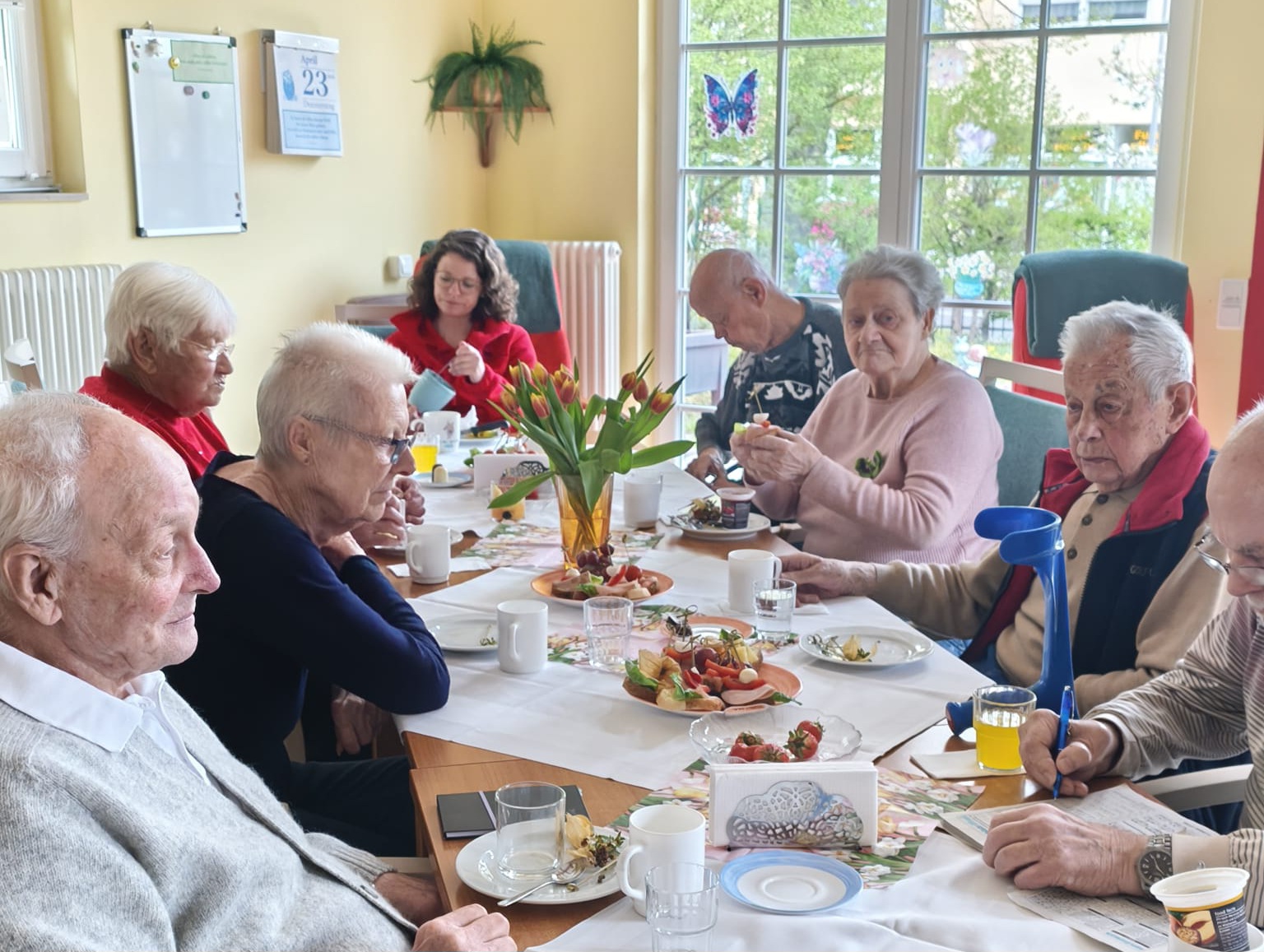 Senioren am Tisch. Essen, Getränke, ein Tulpenstrauß stehen auf dem Tisch.