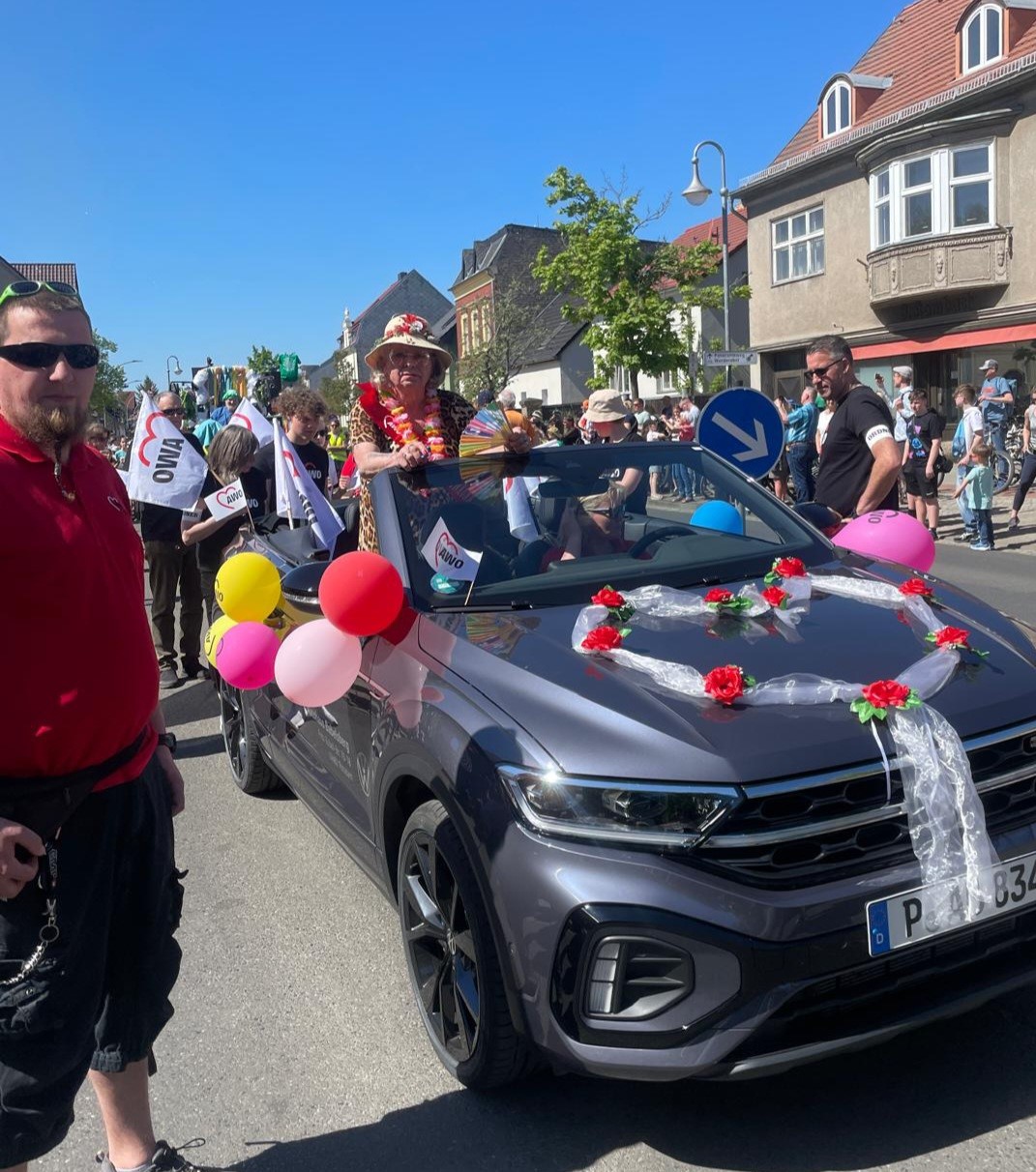 Geschmücktes Cabrio mit Luftballons und AWO Fahnen. Viele Menschen auf der Straße.