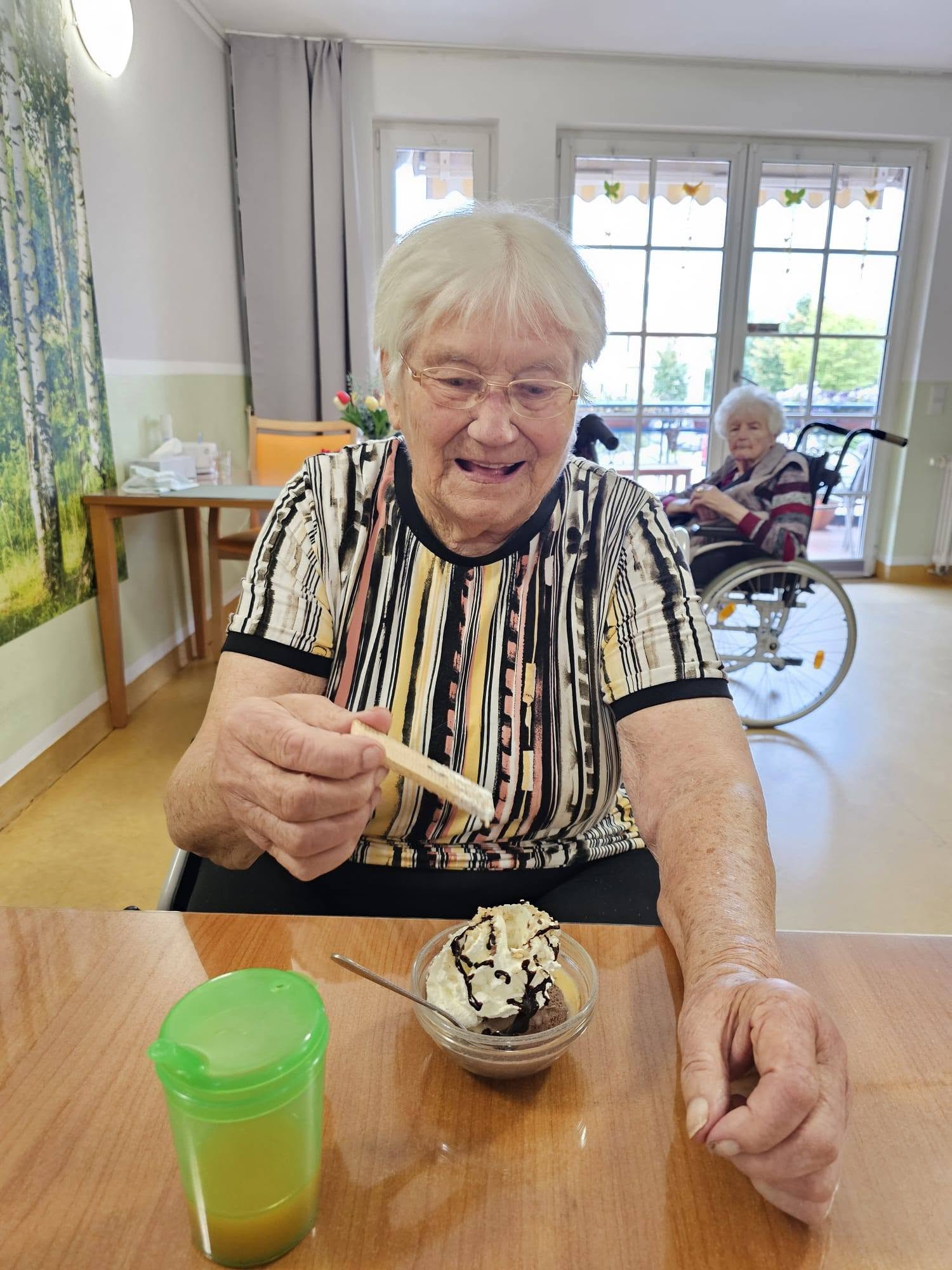 Gutgelaunte Seniorin isst die Waffel mit Schlagsahne. Eisbecher steht vor ihr.
