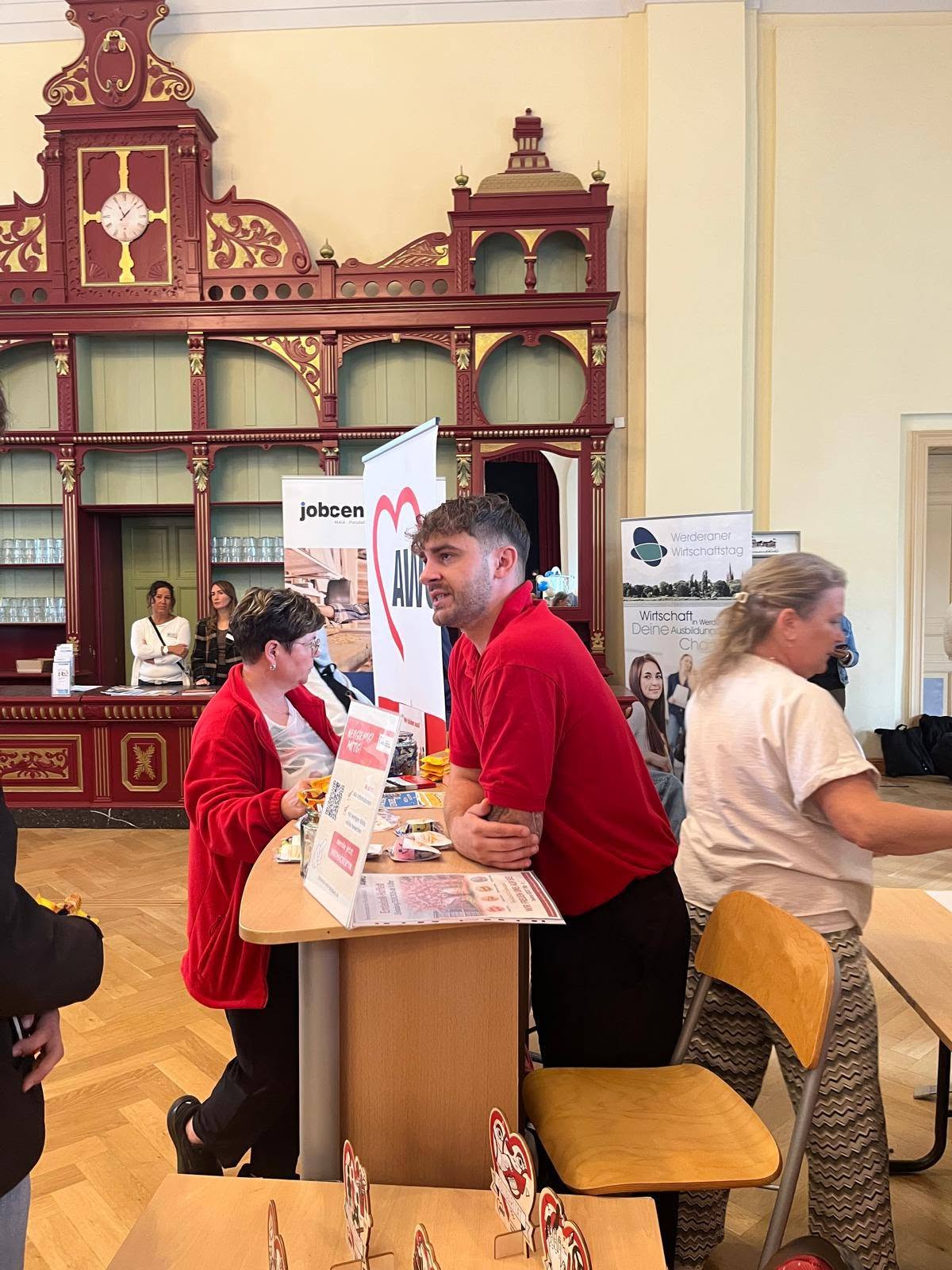 AWO Stand in einem Raum, Mitarbeiter steht am Stand und wartet auf Interessierte Besucher.
