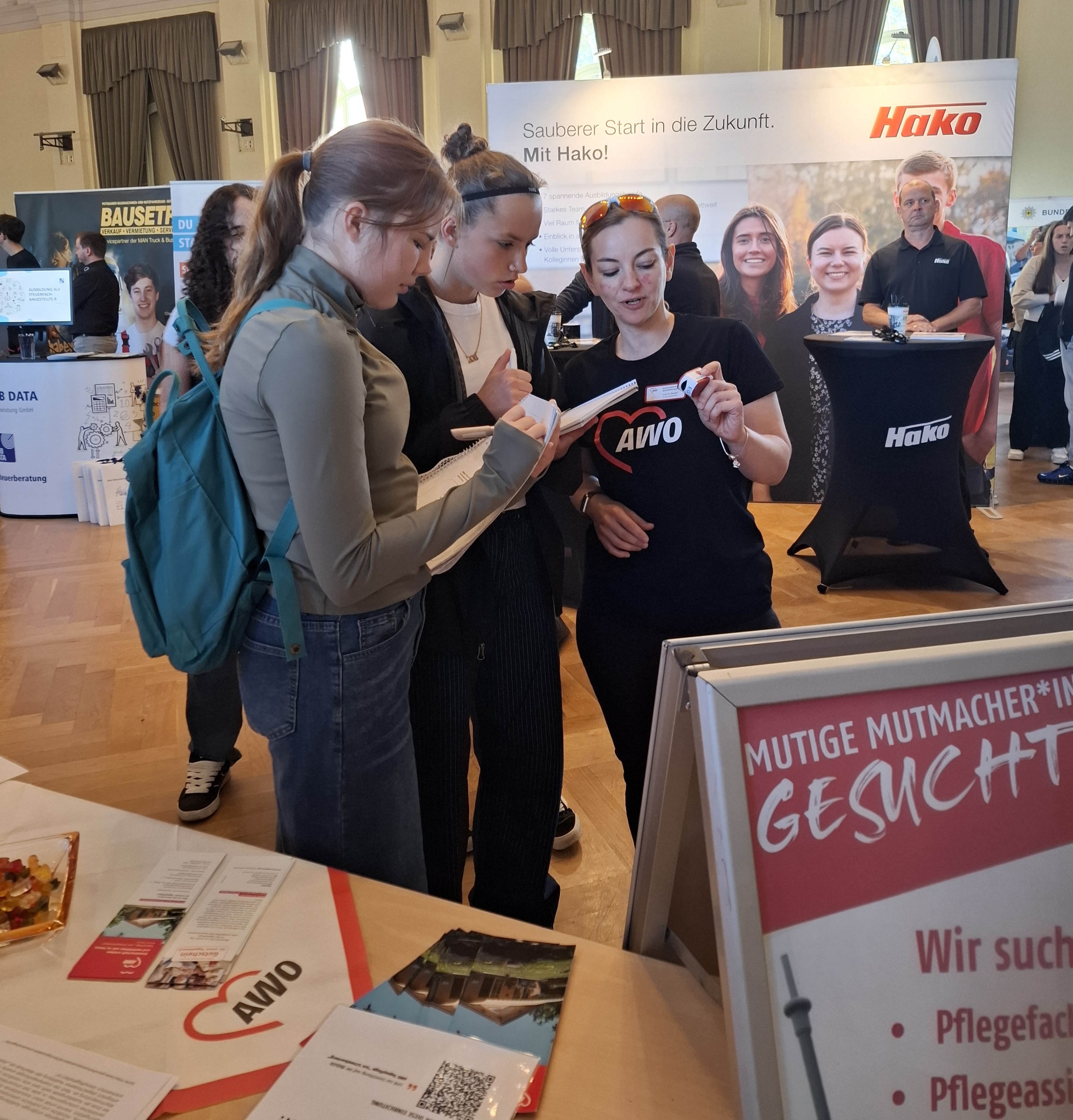 Junge Frauen am AWO Stand, Mitarbeiterin mit AWO T-Shirt informiert.
