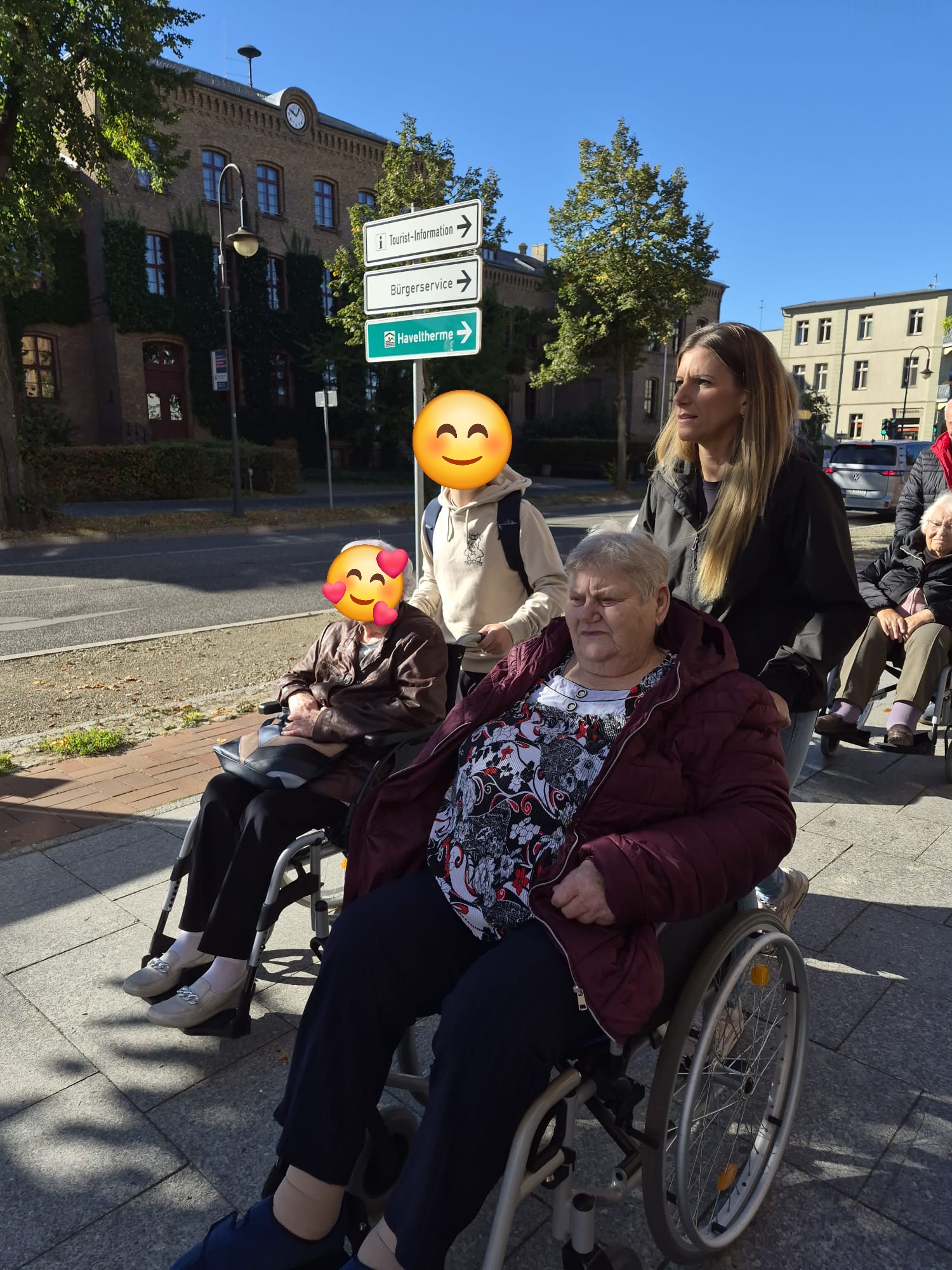 Seniorinnen werden im Rollstuhl auf einem Gehweg geschoben.