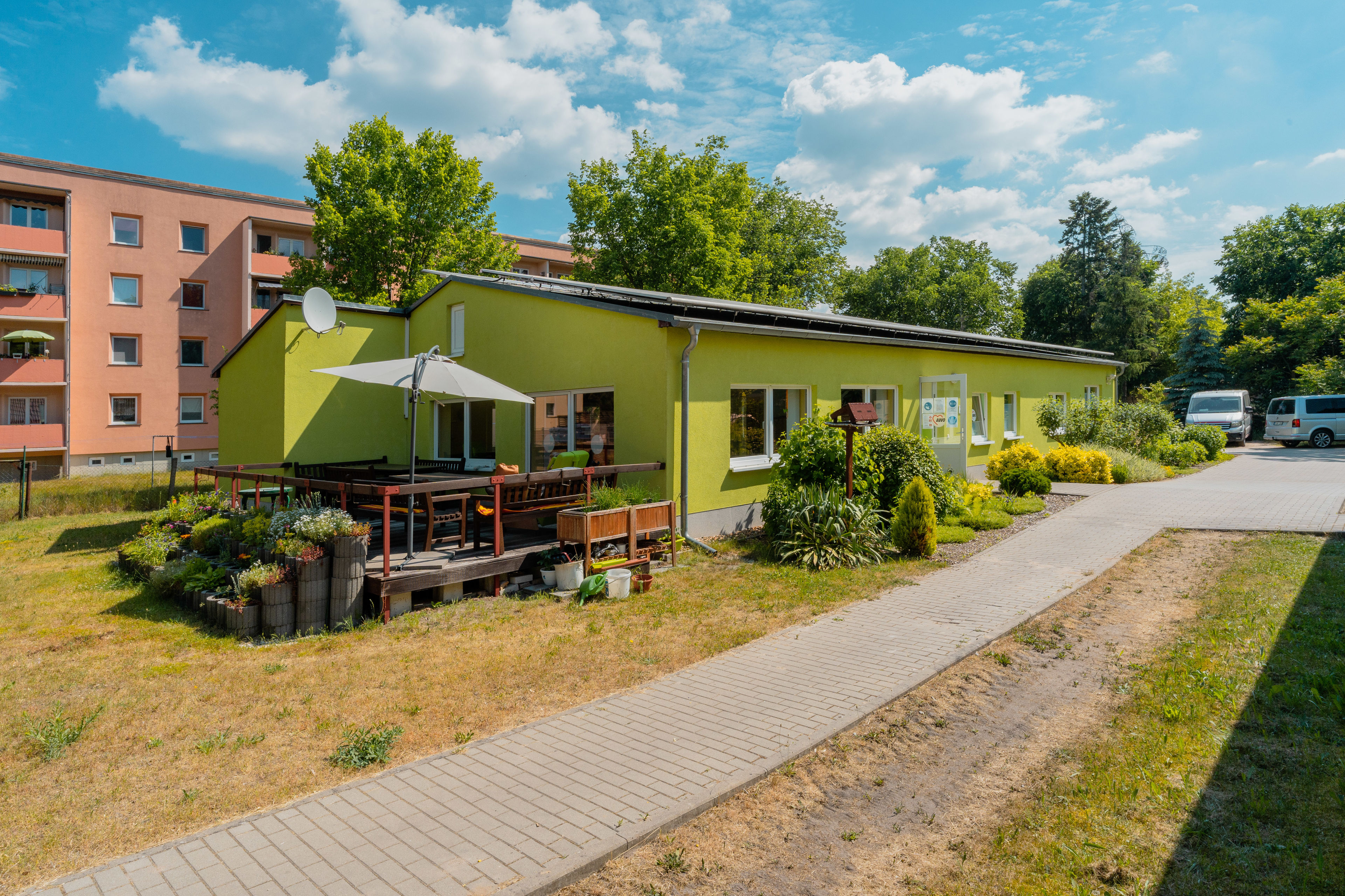 Grüner Flachbau mit einer Terrasse mit Sonnenschirm und Bepflanzung.