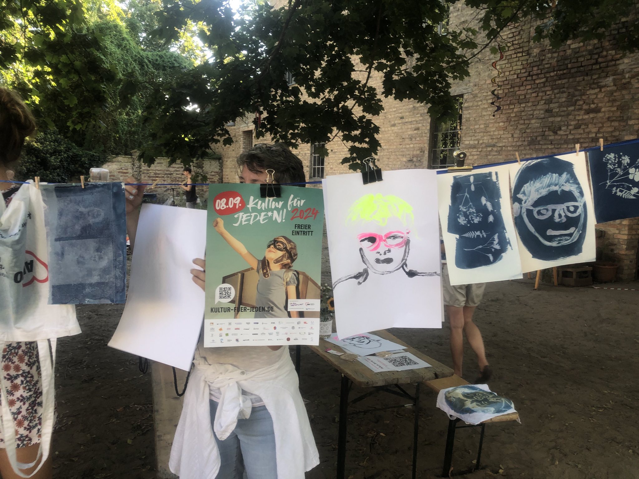 Bilder, AWO Beutel und ein Plakat von Kultur für jeden 2024 hängen an einer Wäscheleine.