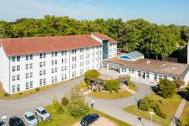 Großes weißes Gebäude mit Parkplatz und Grünflüche davor.