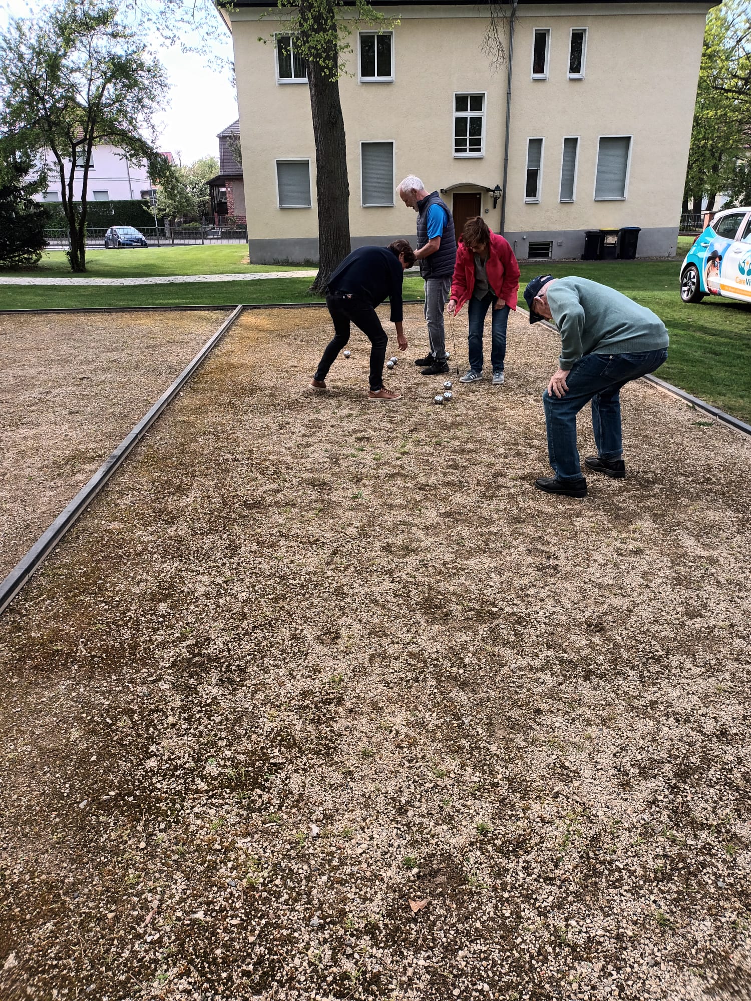 Boule Bahn auf einem gepflegten Grundstück, vier Menschen beim Spielen.