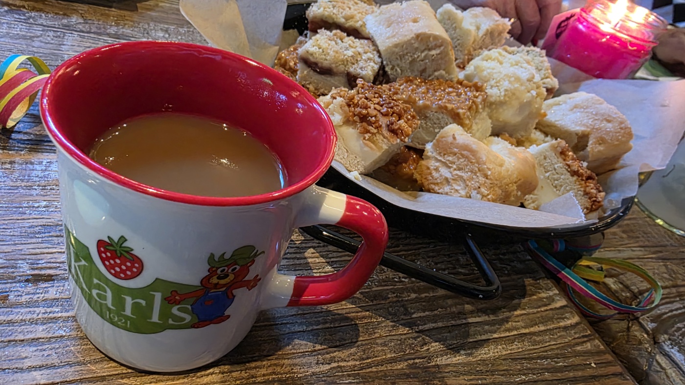 Kaffee in einer Tasse vom Karls Erlebnishof und ein Teller mit Kuchenstücken.