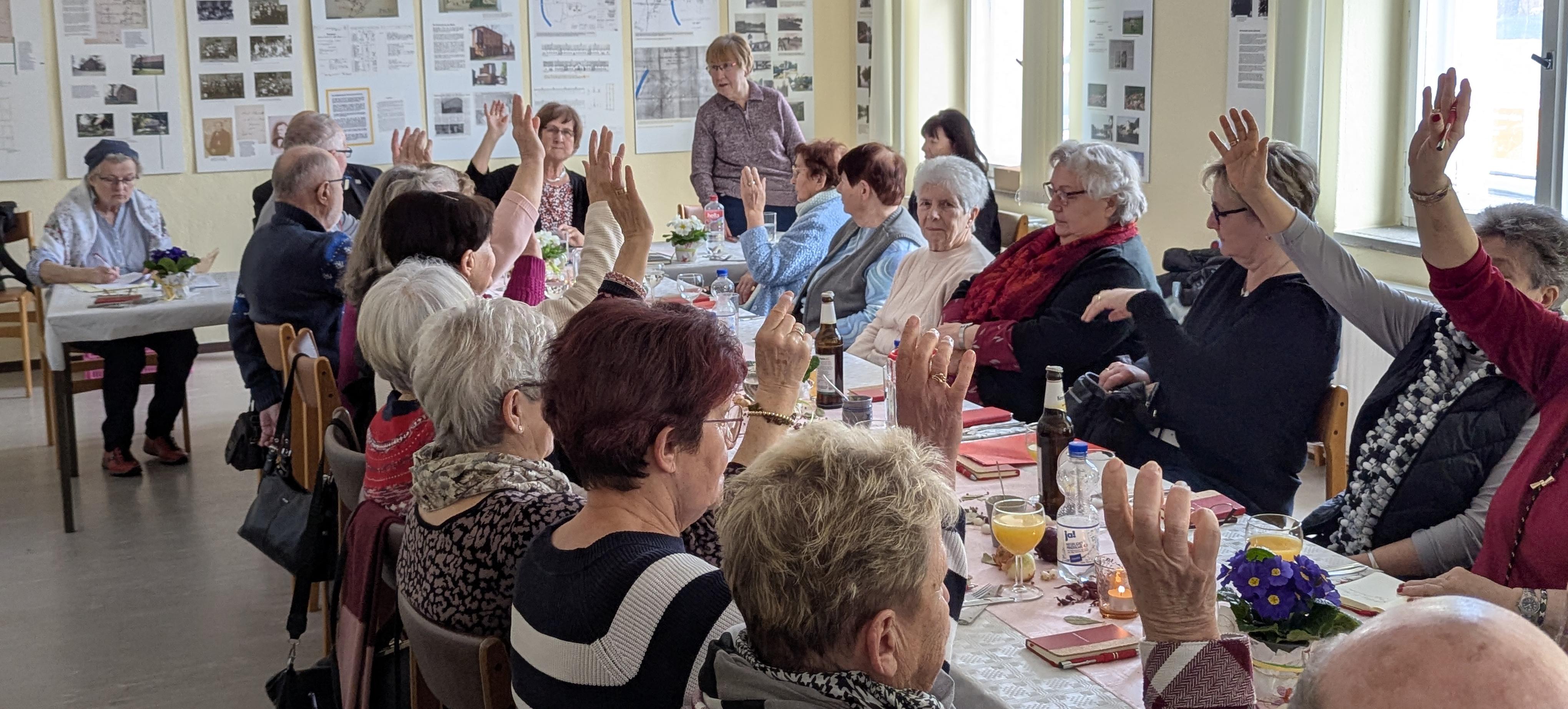 Offene Abstimmung mit Handzeichen. Menschen sitzen an einem langen Tisch.