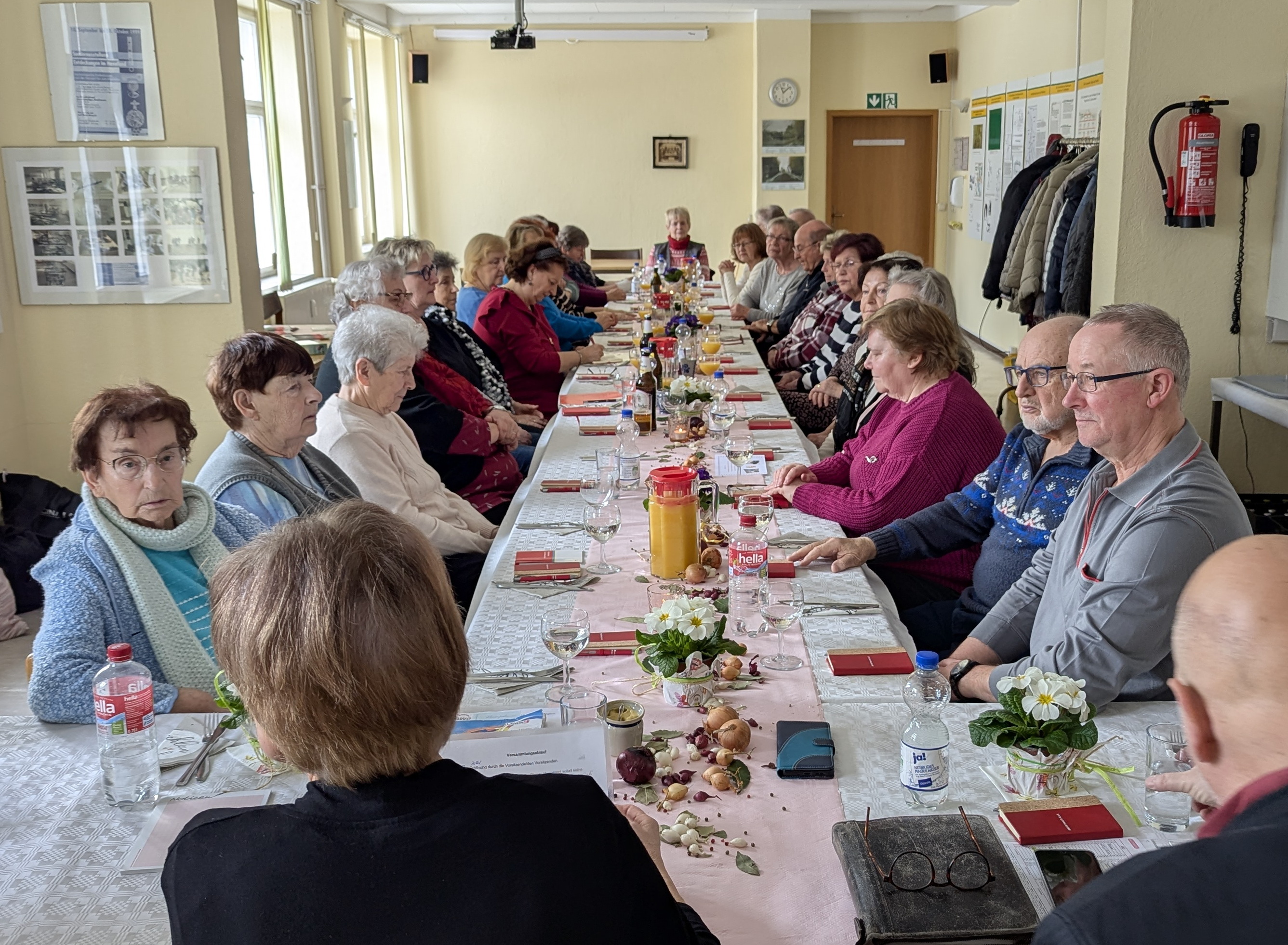 Lange Tafel in T-Form. Viele Machen sitzen an Tisch. Der Tisch ist gedeckt und dekoriert.