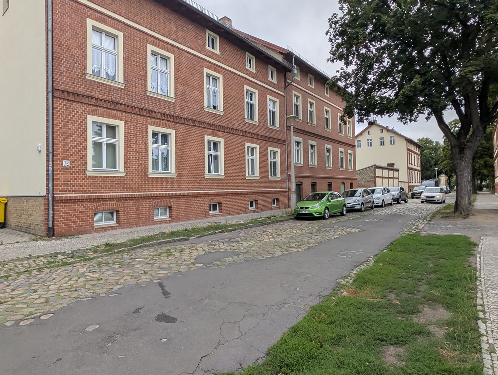 Haus, schmaler Gehweg und alte Straße zum Teil Kopfsteinpflaster zum Teil Ausfalt.