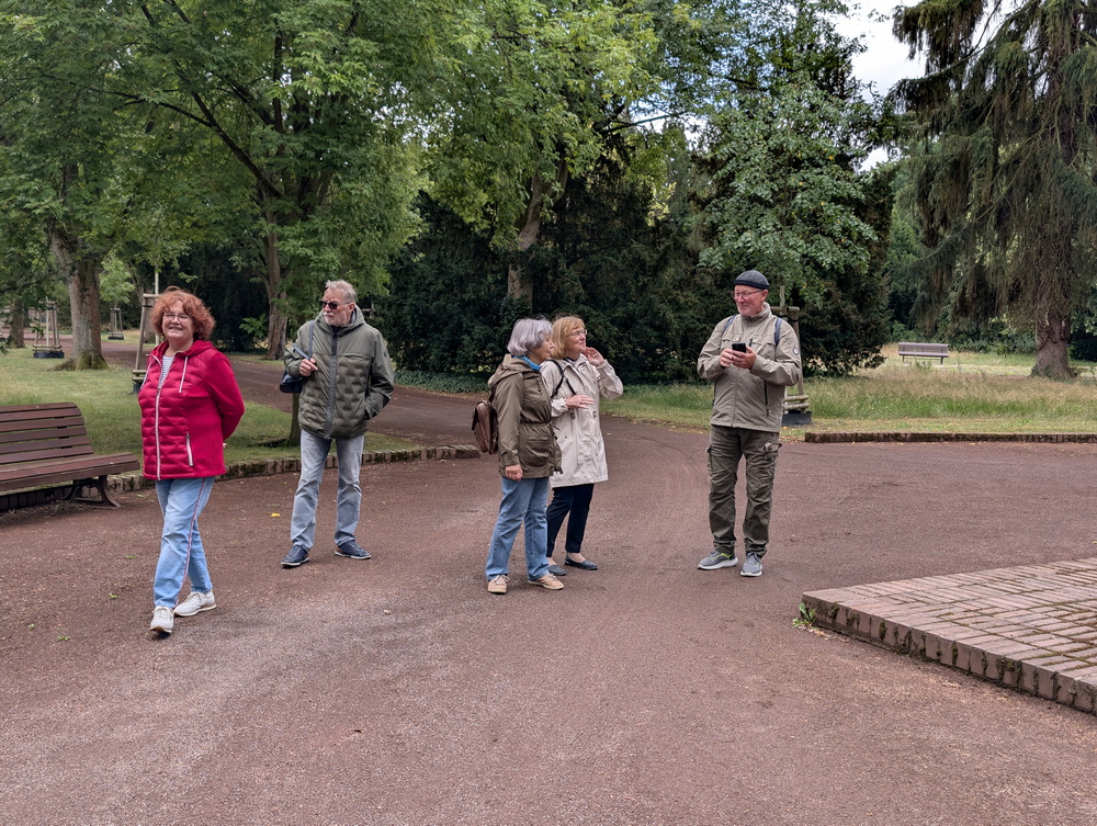 5 Mitglieder der Wandergruppe auf einem Platz. Dahinter ein Weg gesäumt von Bäumen.
