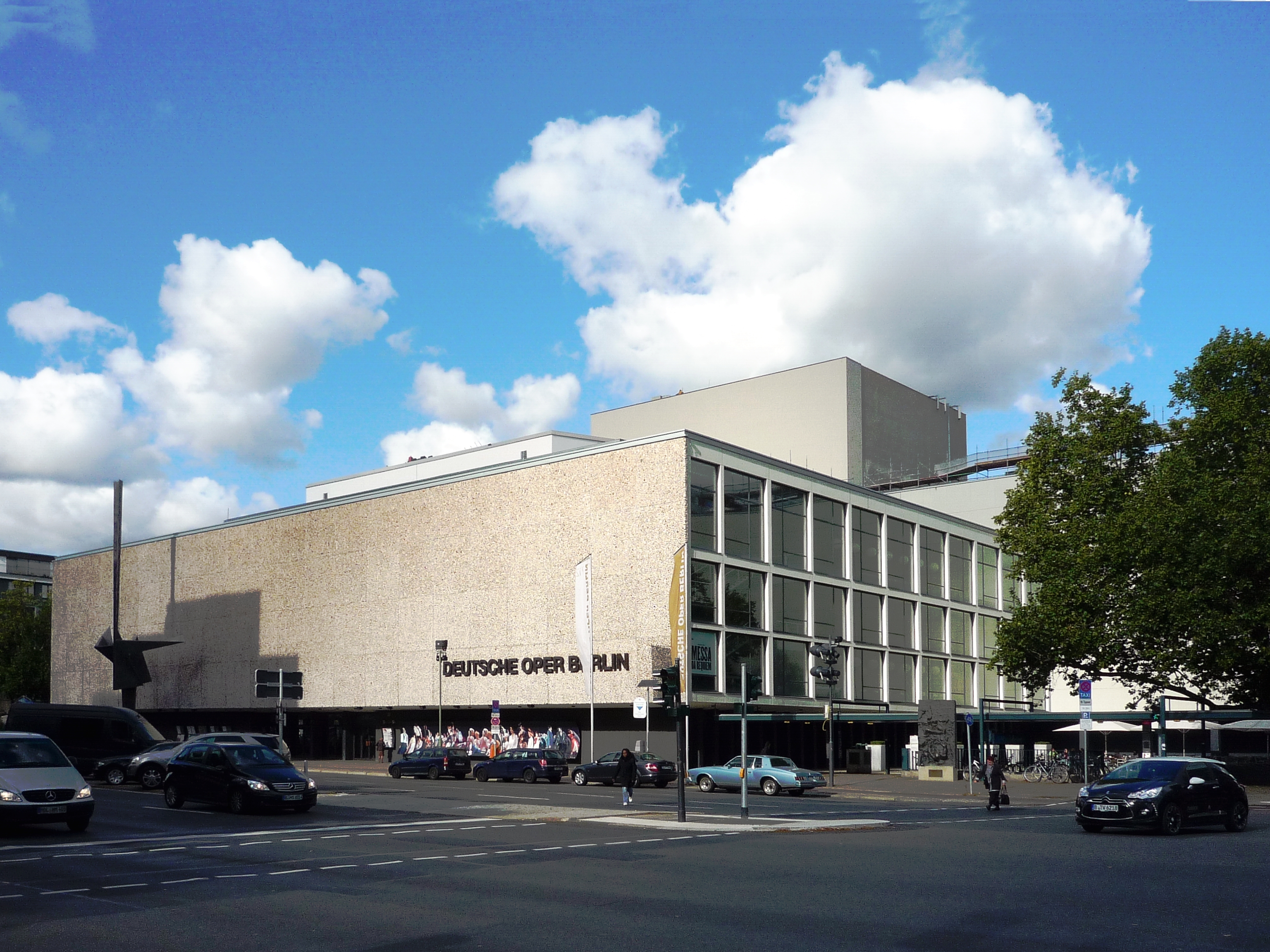 Deutsche Oper Berlin. Ansicht von Südosten. Von der anderen Straßenseite fotografiert. Menschen stehen vor der Oper.